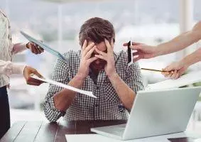 Mann vor einem Laptop mit Handy, Tablet und Papier, der kurz vor einem Burnout steht.